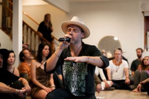 A performer in a cowboy hat sings into a microphone while an audience sits and watches attentively.