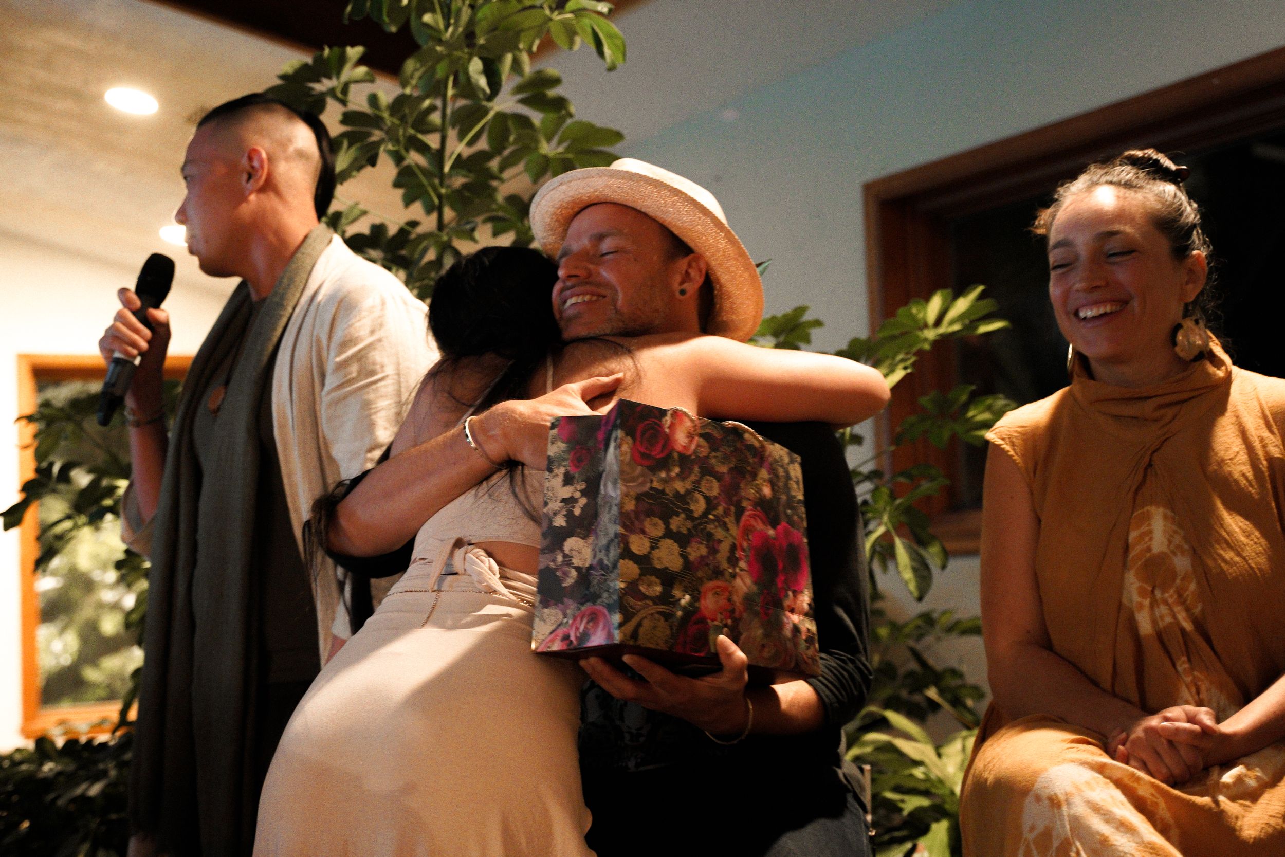 People sharing a candid moment during an indoor event with microphones and plants visible.
