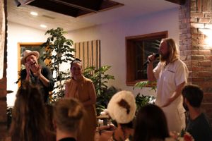 A performance takes place in a restaurant setting with plants and brick walls visible in the background.