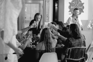 A black and white photo of people gathered around a table raising drinks in celebration.