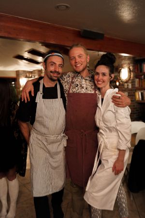 Restaurant workers pose together in a warm-lit space wearing aprons and professional attire.
