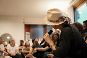 Person in a cowboy hat speaks into microphone during an intimate gathering.
