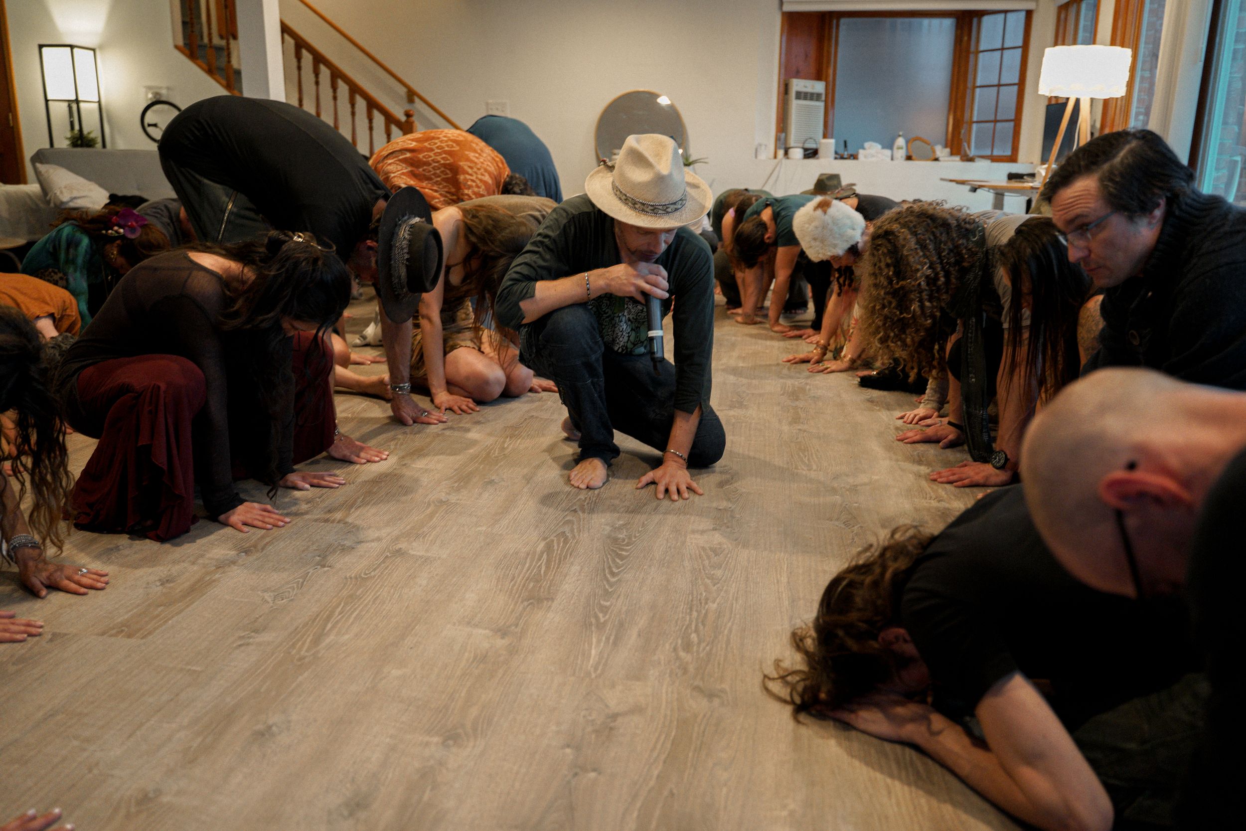 A group of people bend forward in unison during what appears to be a dance or movement exercise.