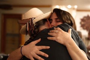 Two people share an emotional embrace at an indoor gathering.