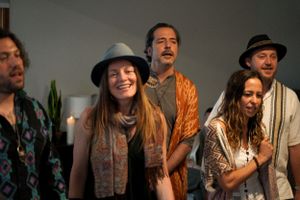Performers in bohemian style clothing and hats gather for a group performance.