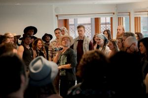 Crowded room of performers and audience members sharing an intimate musical moment.