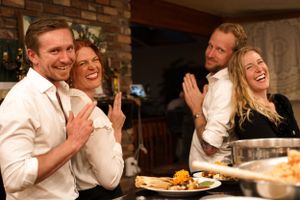 Two couples share joyful laughter during a dinner gathering.