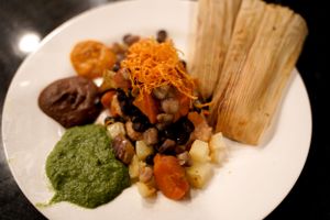 A plated dish with tamale, colorful sauces, and garnishes on a black plate.