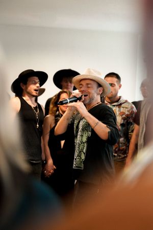 Performer in a cowboy hat singing passionately into a microphone surrounded by audience members.