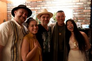 A group poses together at an indoor event wearing casual attire and hats.