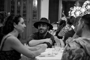 A casual dining scene in black and white with guests seated at a table in conversation.