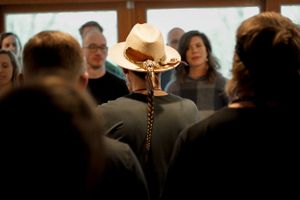 View of a cowboy hat from behind in a crowded indoor setting with wooden window frames.