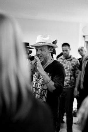 Person in a cowboy hat and casual attire speaking into a microphone among a crowd.