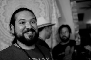A black and white portrait of someone smiling warmly at an indoor gathering.