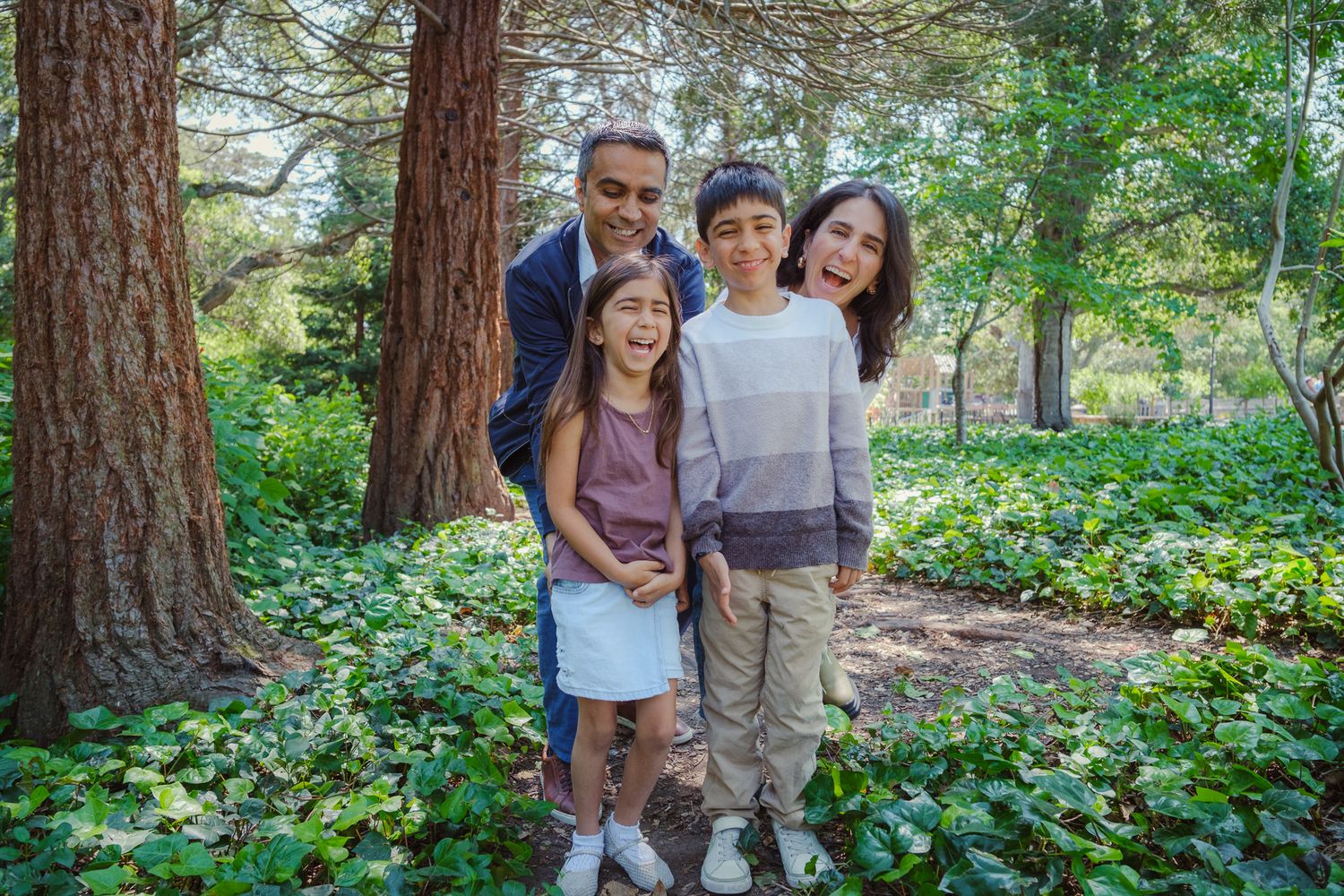 Happy family group enjoys spending time together while posing outdoors in a lush forest garden setting.