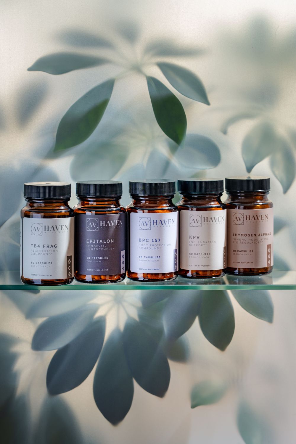 Five amber glass supplement bottles lined up on glass shelf with soft green leaf shadows in background.