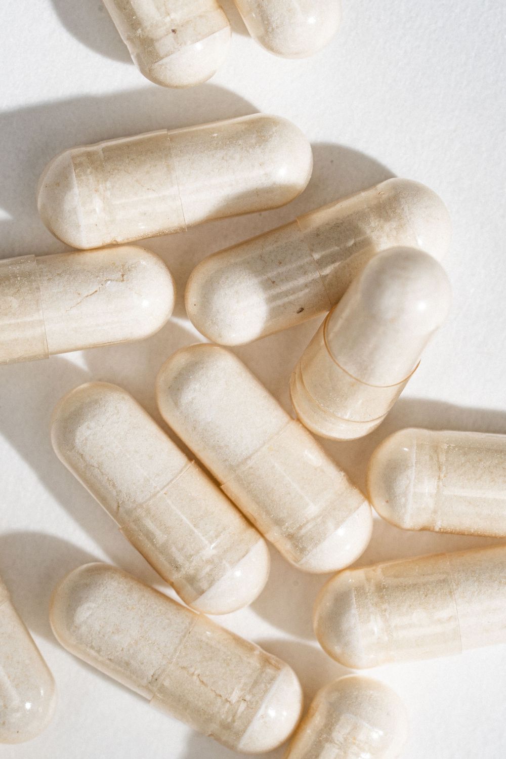 Close-up view of white pharmaceutical capsules or supplements scattered on a light surface with dramatic shadows.