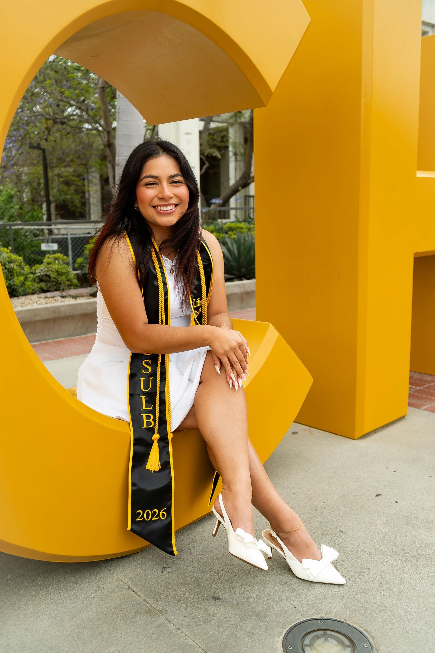Graduate in cap and gown stands on campus steps wearing a Cal State LA stole.