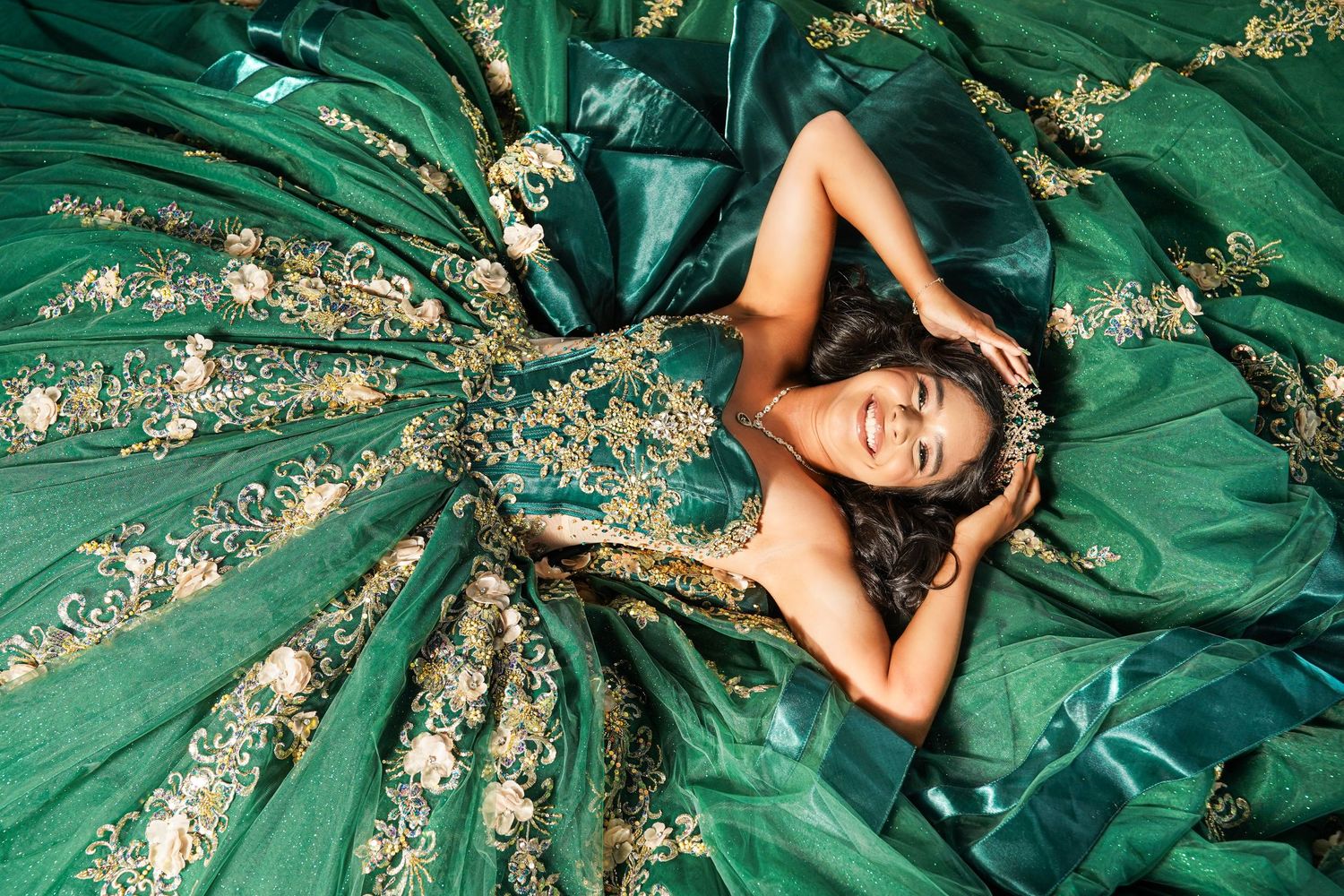 Young woman lying in an elegant emerald green ball gown with gold embroidery details spread around her.