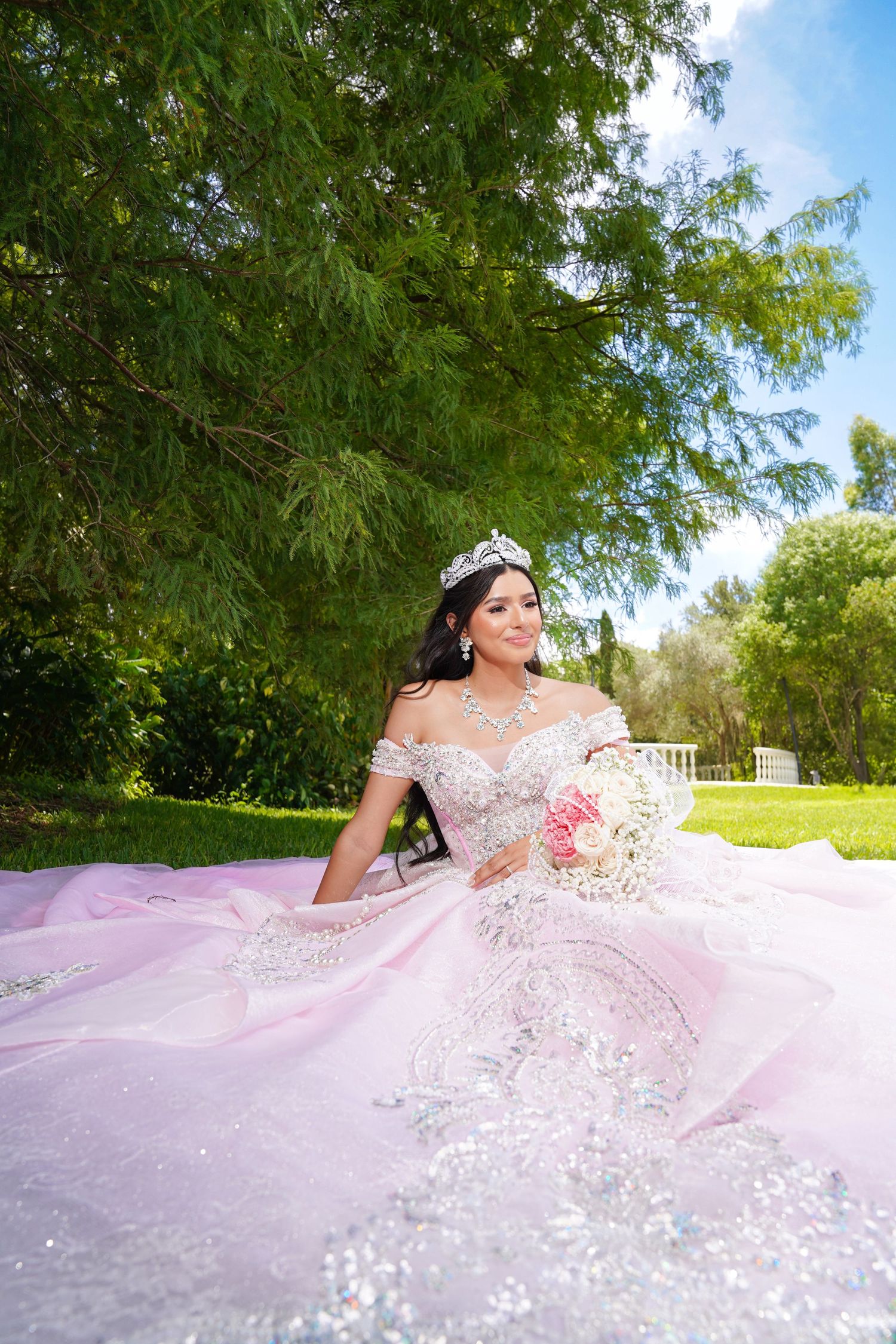 Pink princess ball gown photographed in garden setting with blooming trees.