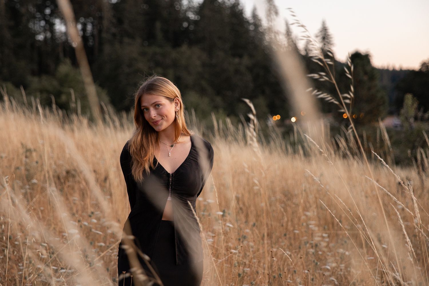Young woman in a black dress posing gracefully in a golden field at dusk.