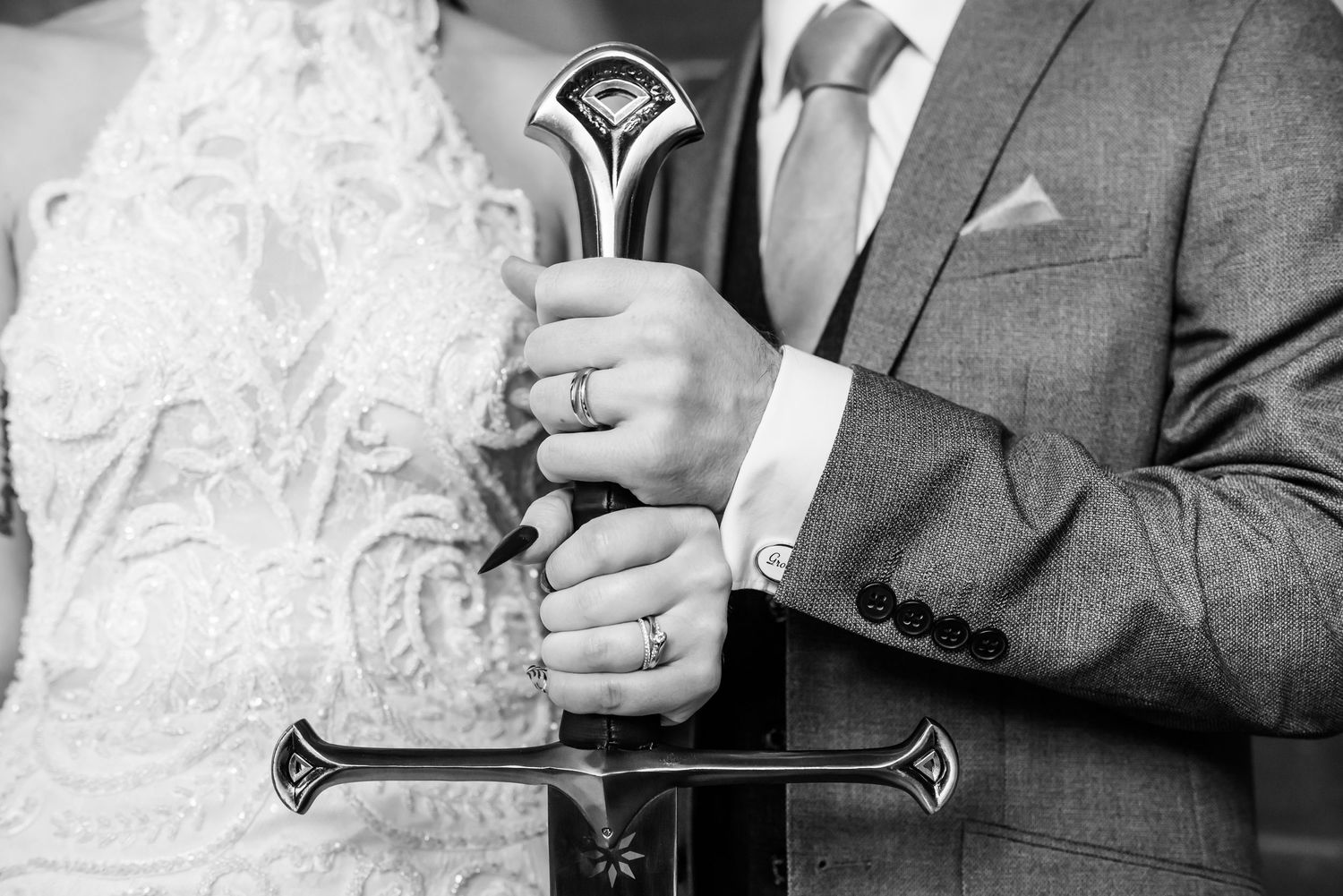Close-up black and white photo of hands holding an ornate ceremonial sword with detailed hilt at a wedding ceremony.