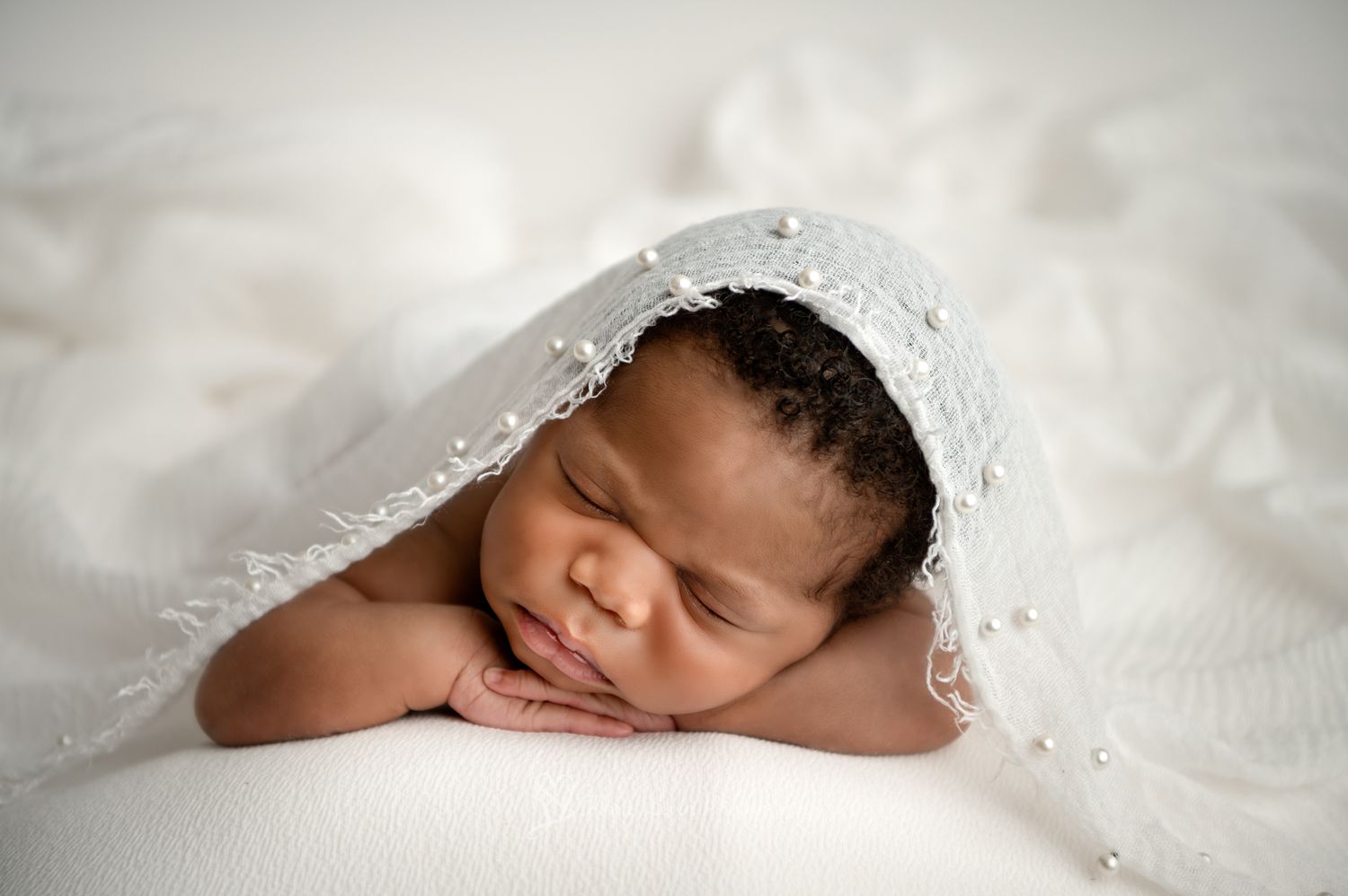 A newborn baby swaddled in soft white lace fabric sleeps peacefully in natural light.