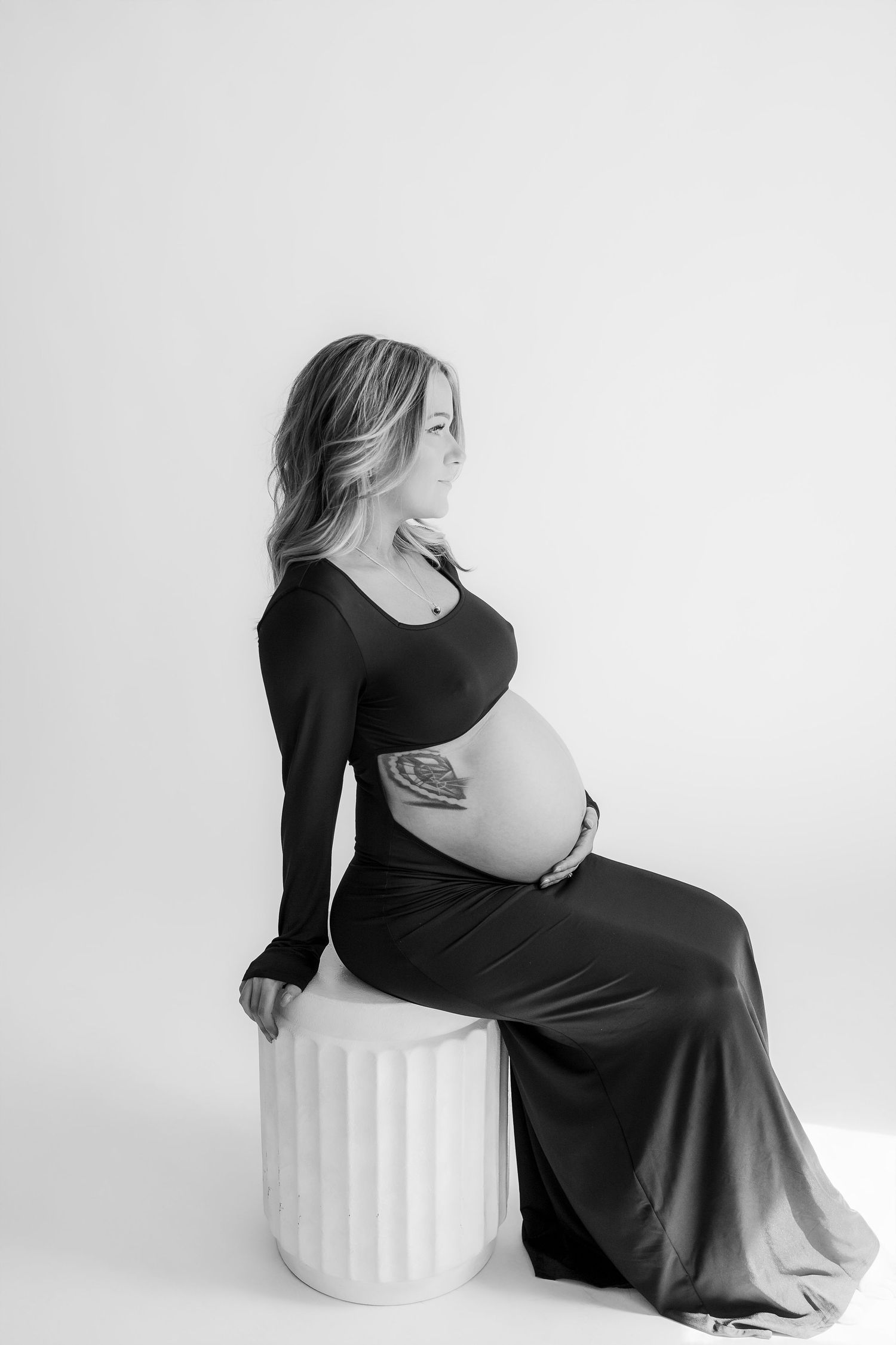 A maternity photo shoot with a couple in black clothing against a white backdrop, featuring tattoos and sunglasses.