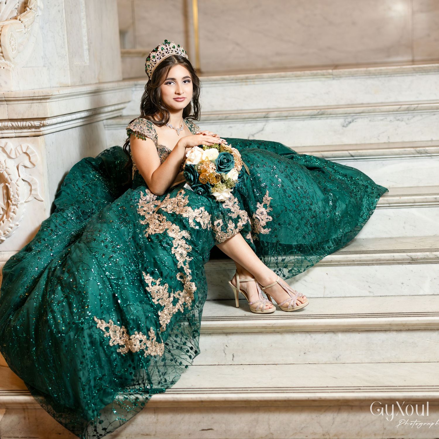A woman in an emerald green lace gown lounges gracefully on marble steps in an elegant setting.