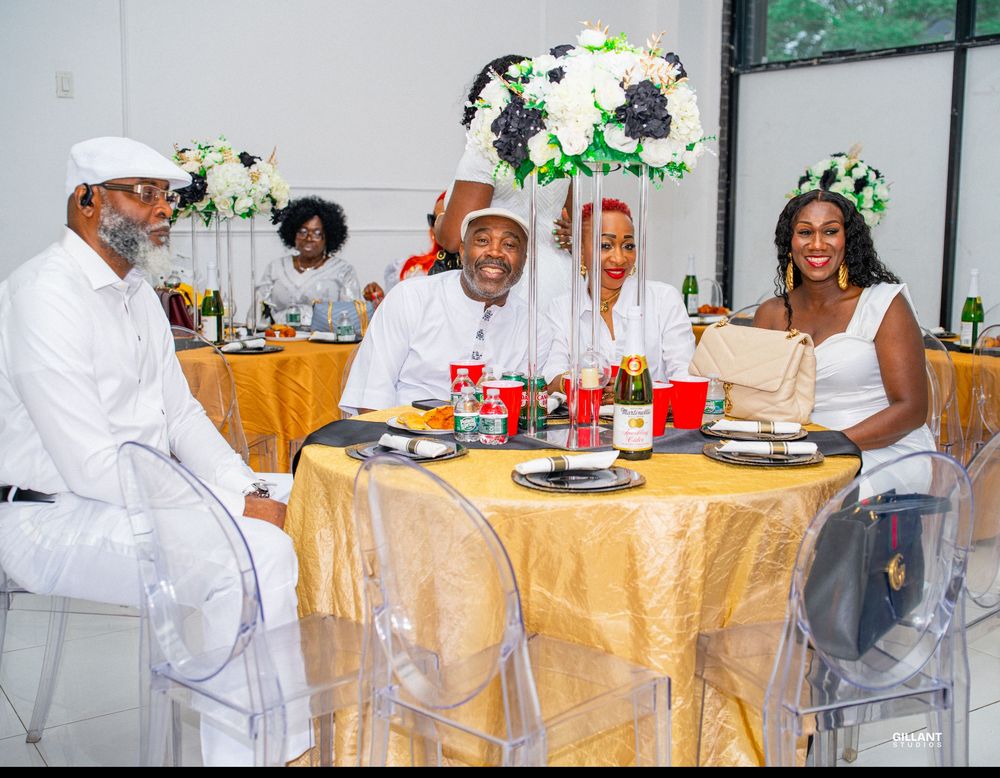 Guests seated at round table with gold tablecloth and white floral centerpiece at formal event.