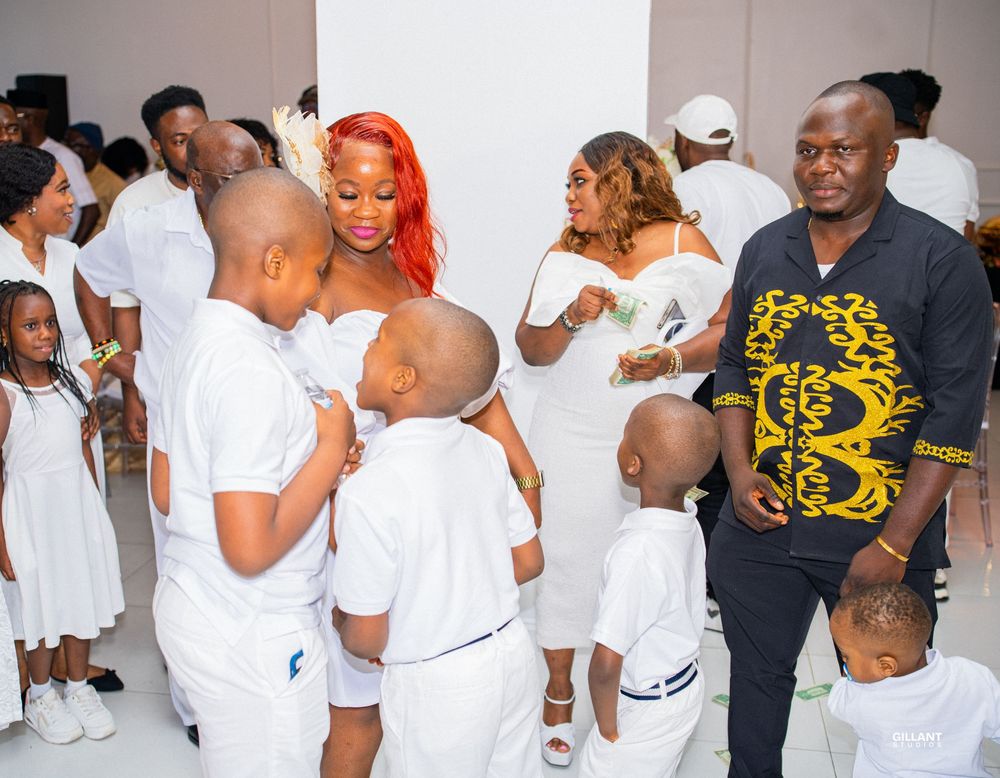 Group in white attire gathered with children at formal celebration event.