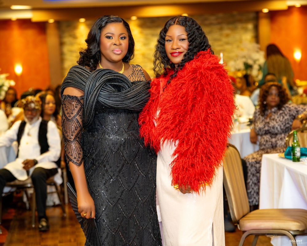 Two women pose at formal event wearing black gown and red feathered wrap.