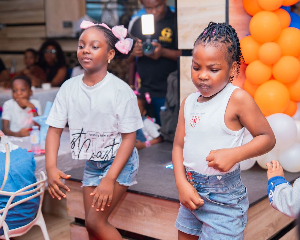 Children playing and dancing at party with orange and blue balloon decorations.