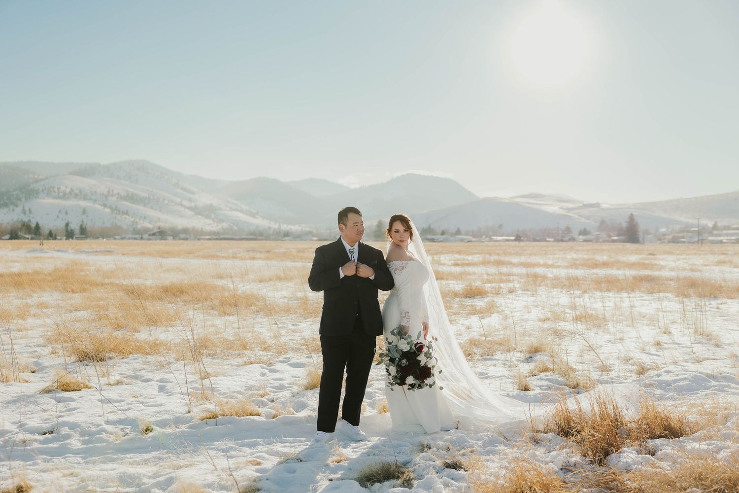 Winter wedding photography in a snow-covered field with mountain views.