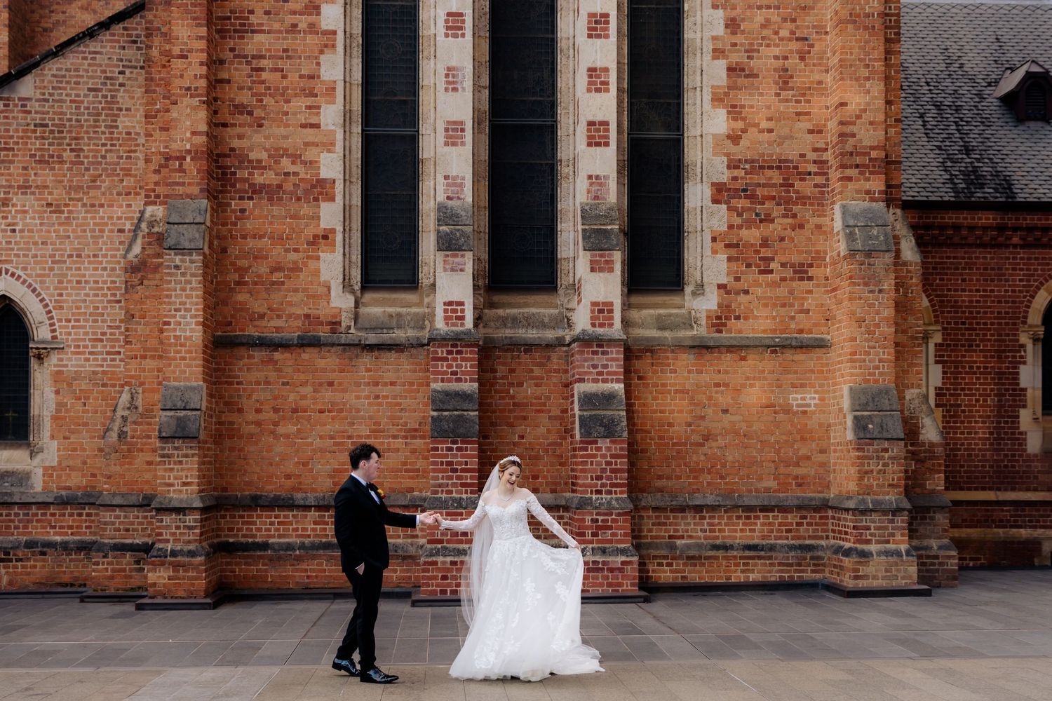 A couple stands in front of a historic brick church facade on their wedding day.