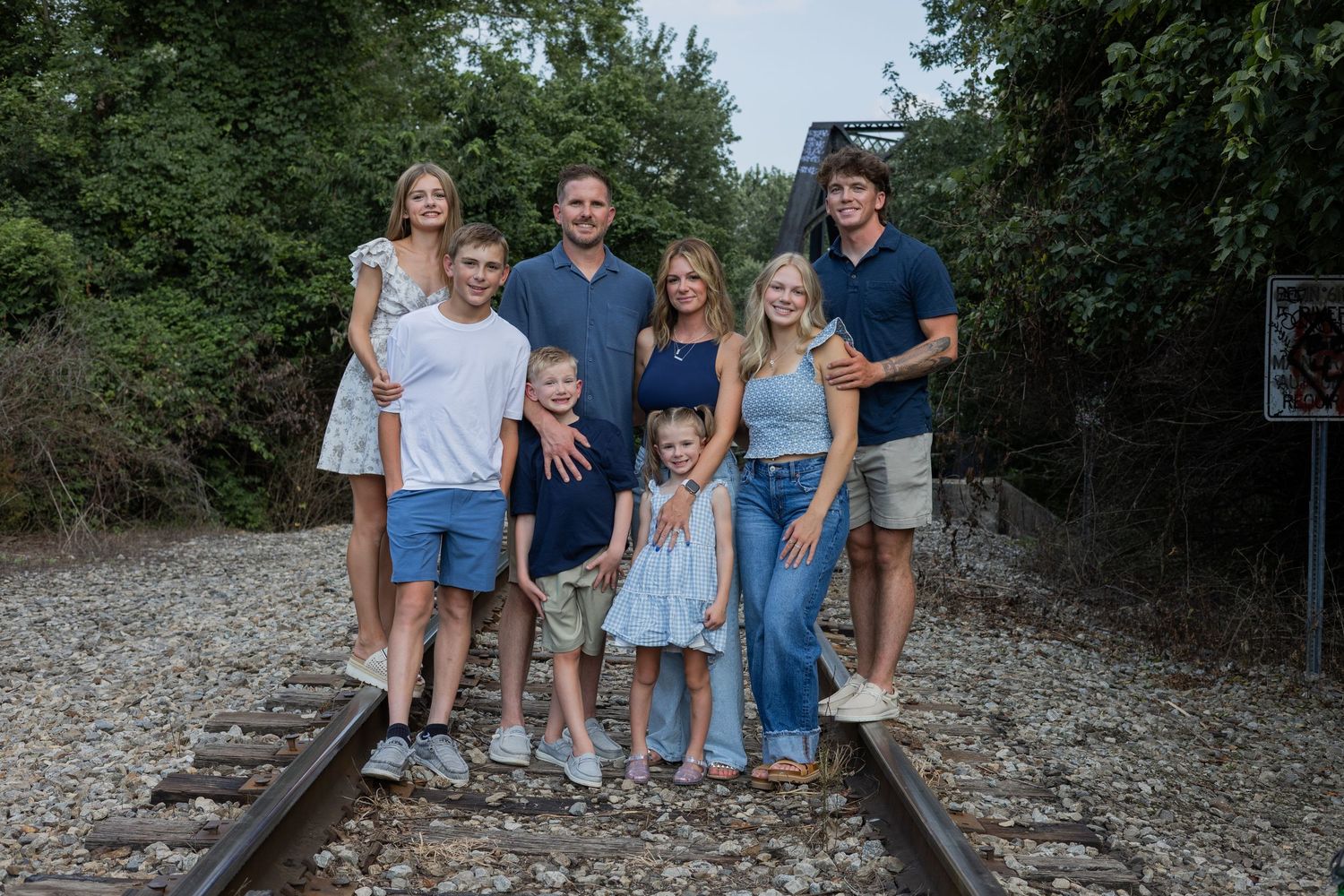Family photo session on rustic railroad tracks surrounded by greenery.