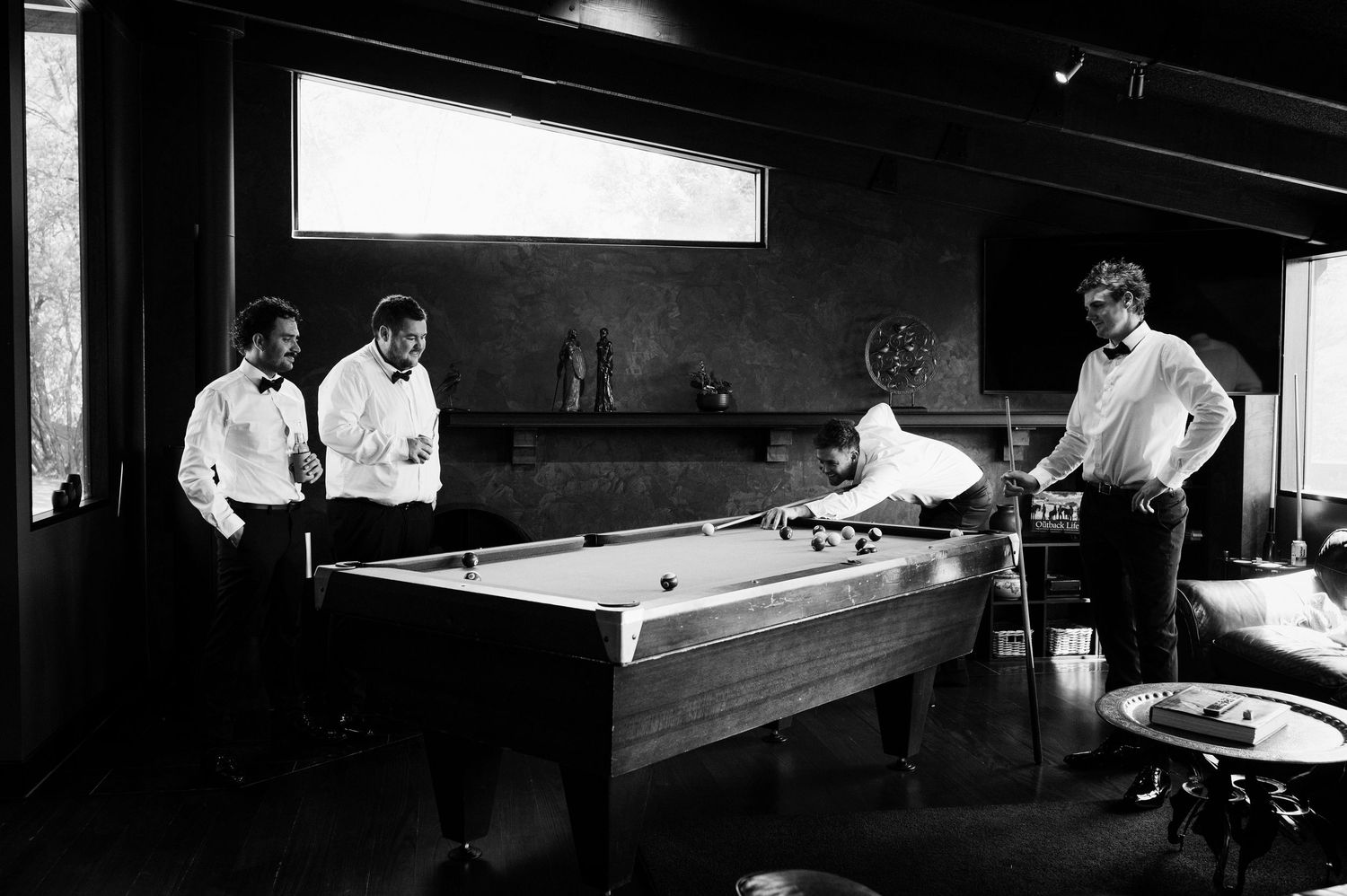 Three people playing a game of billiards at a pool table in a vintage black and white photograph.