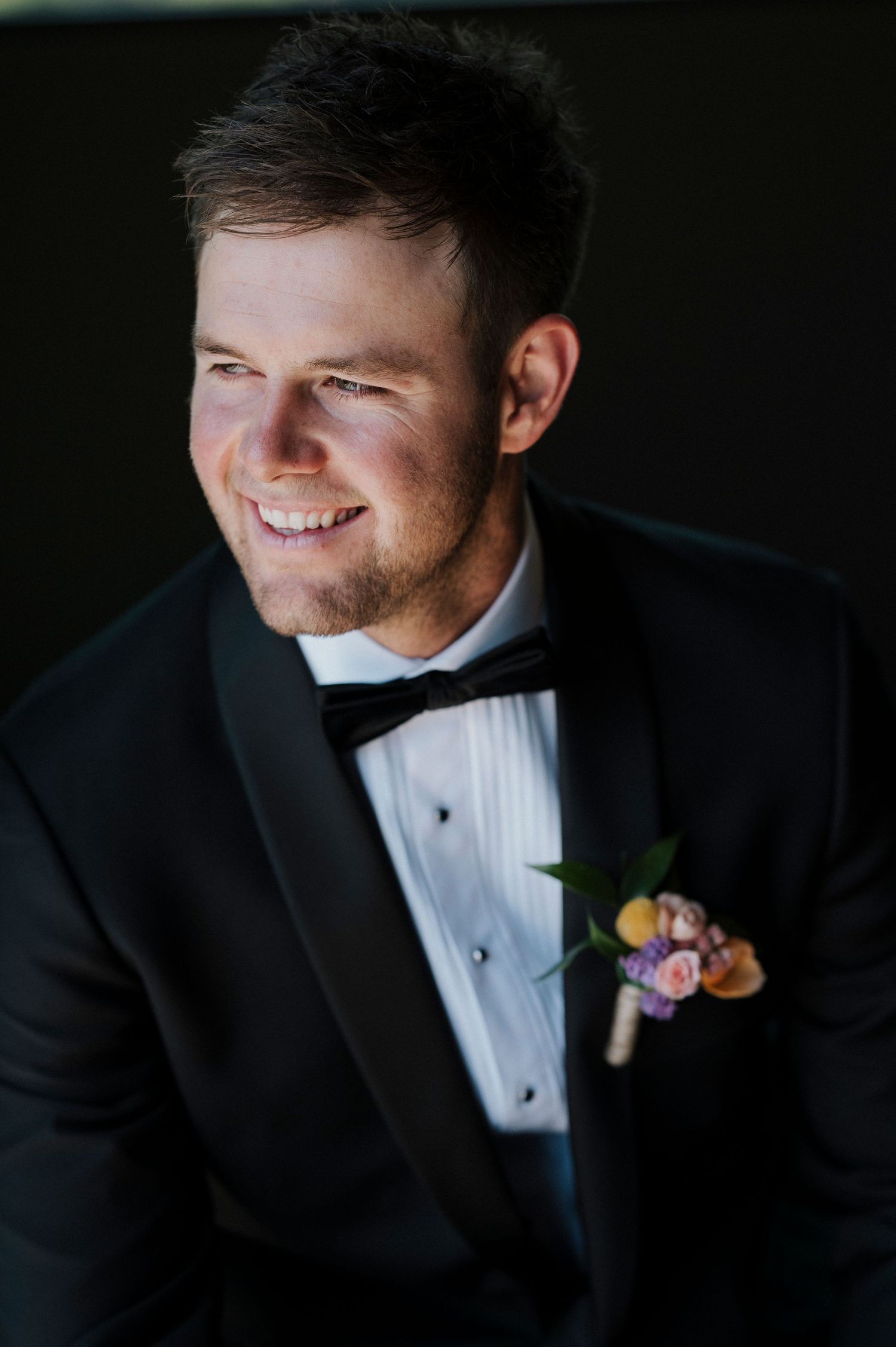 Close up detail shots of a groom in a black tuxedo wearing a pink and purple floral boutonniere.