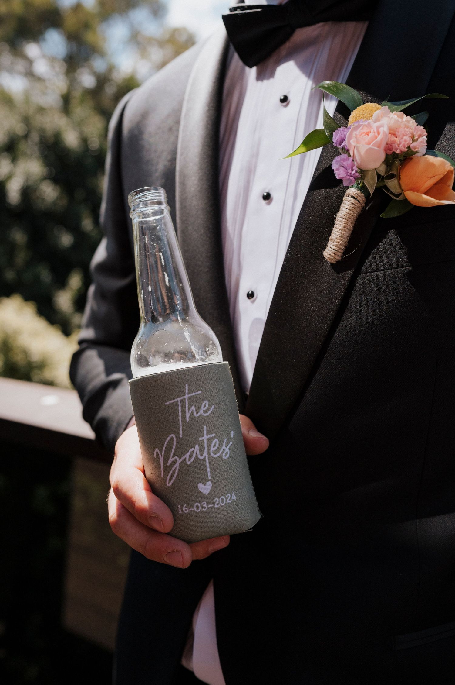 Close-up shots of groom in black tuxedo holding custom etched wedding glasses with formal attire and floral boutonniere.