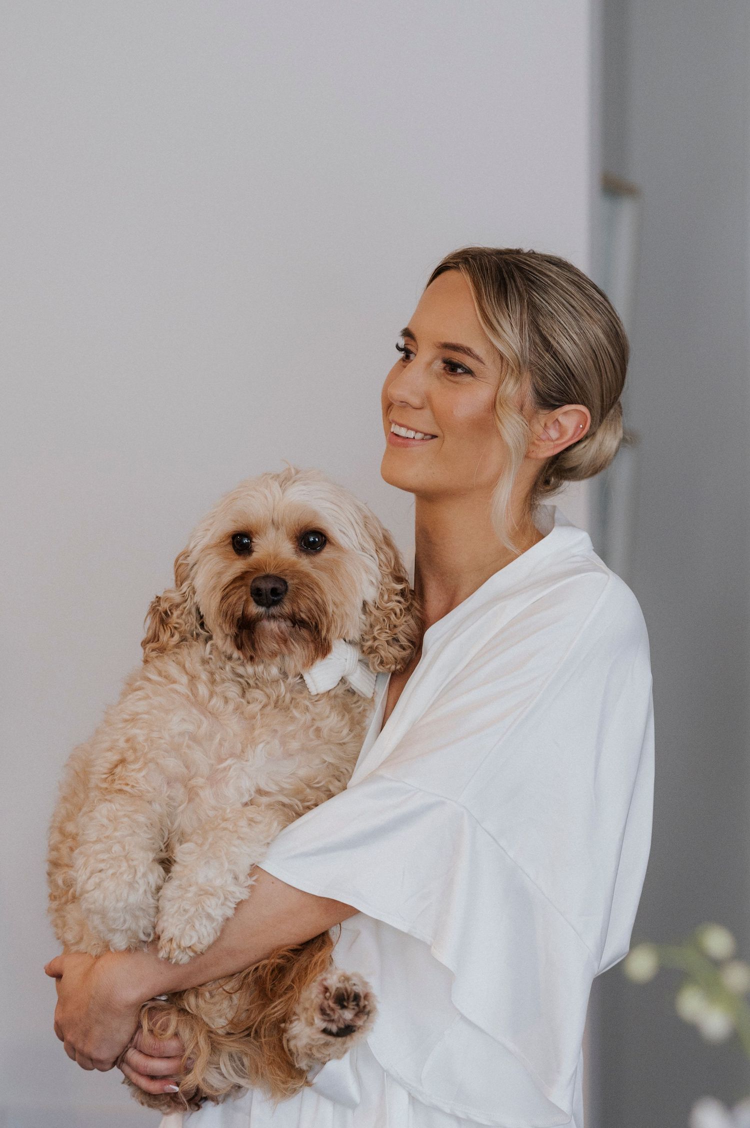 A person in a white shirt holding an adorable fluffy cream-colored Cavapoo or similar mixed breed dog.