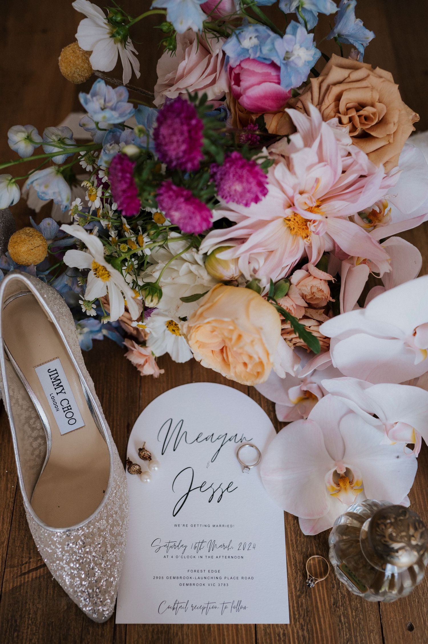 Wedding invitation with sparkly Jimmy Choo shoes and romantic floral bouquet featuring roses and orchids on wooden surface.