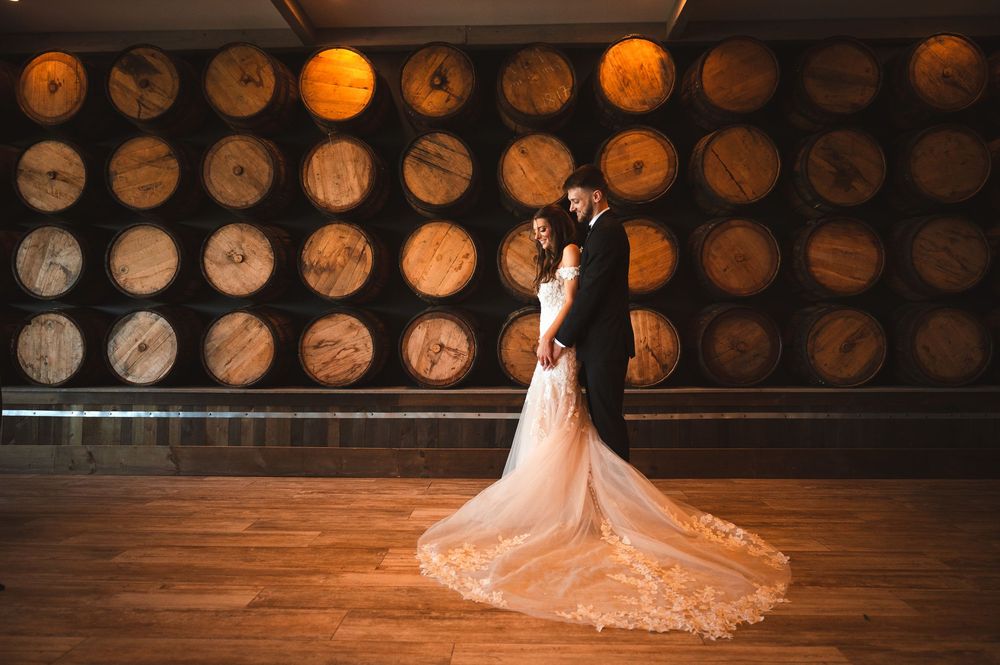 Wedding couple poses in rustic winery cellar with wooden barrels lining the wall behind them at the Barn at Villa Venezia Middletown.