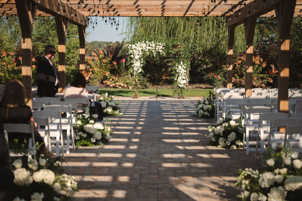 Outdoor garden wedding ceremony setup with white chairs and floral arrangements lining a stone paved aisle at The Barn at Villa Venezia.