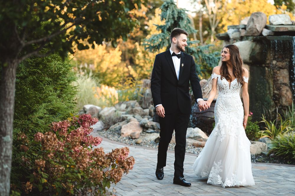 A bride and groom walk together through a garden pathway during golden hour at The Barn at Villa Venezia Middletown.