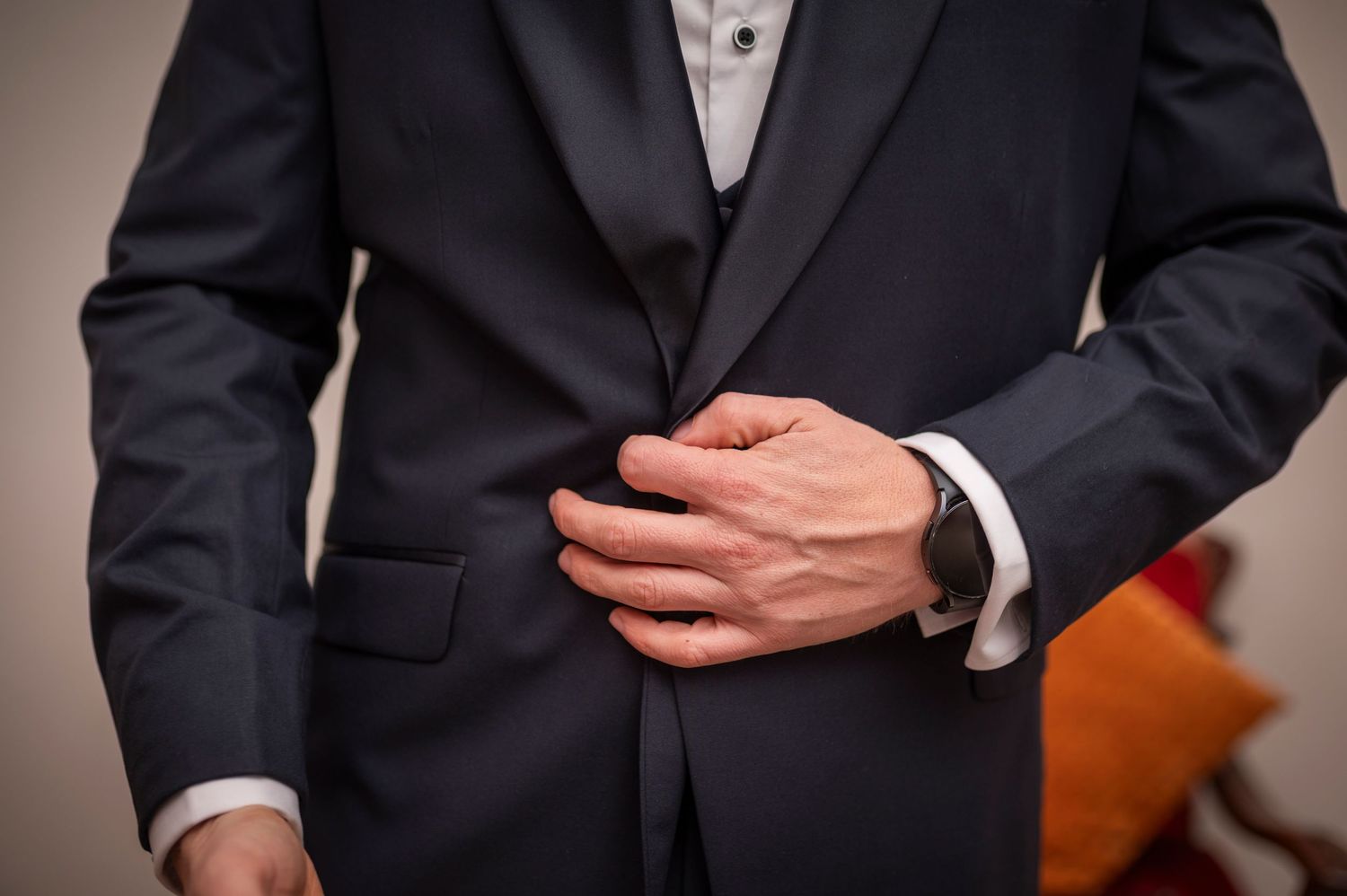 Close-up of person wearing formal black suit and white dress shirt adjusting their jacket button.