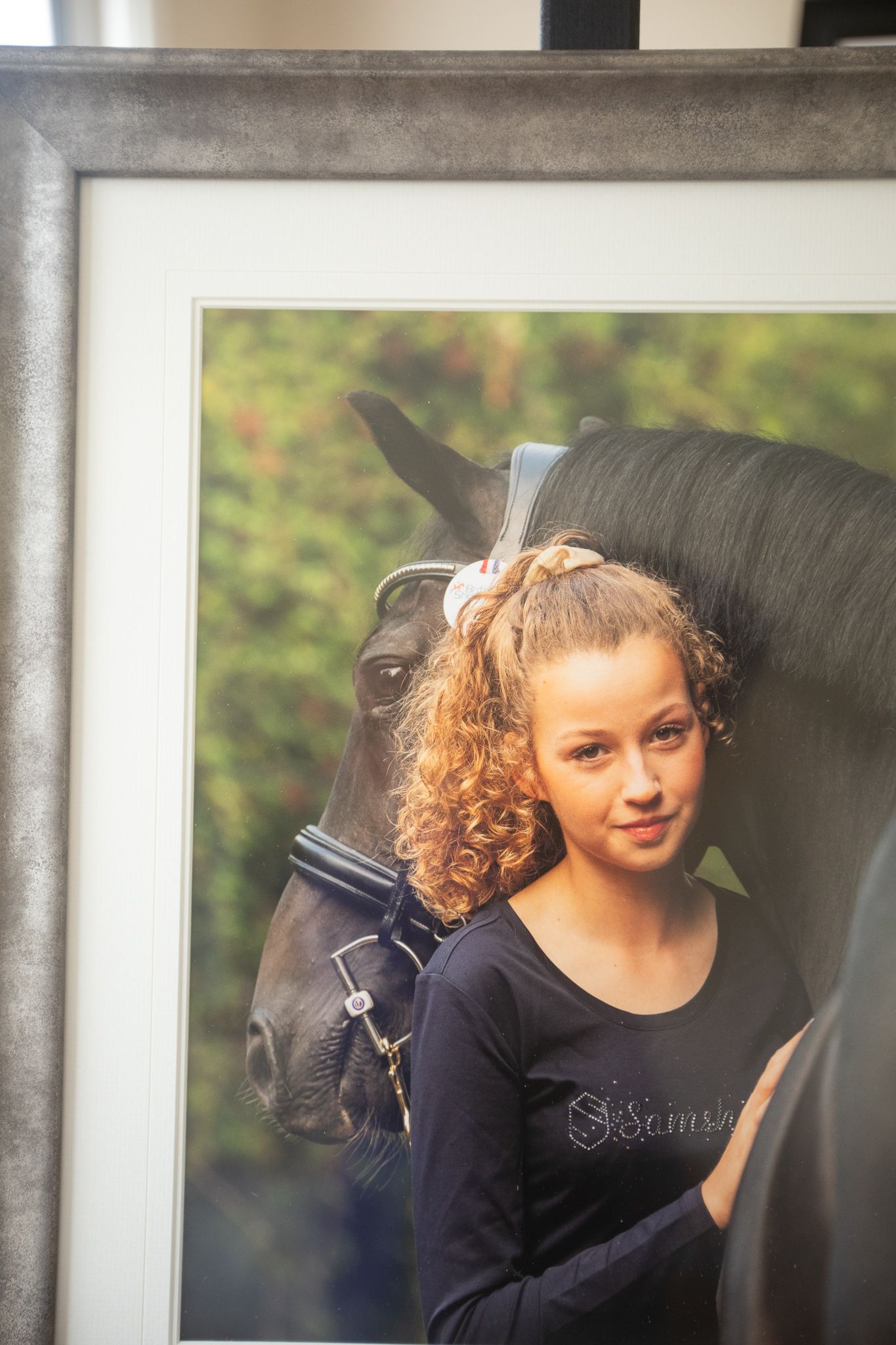 A framed equestrian photo showing a black horse gazing at the camera alongside someone wearing a black top.