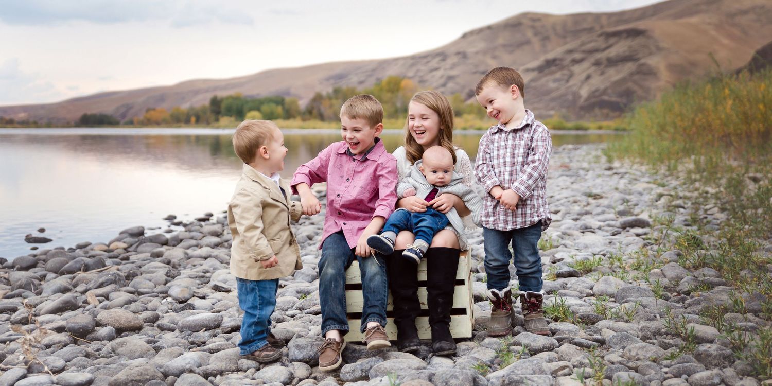 Family group sitting together on rocky terrain with mountains in background.