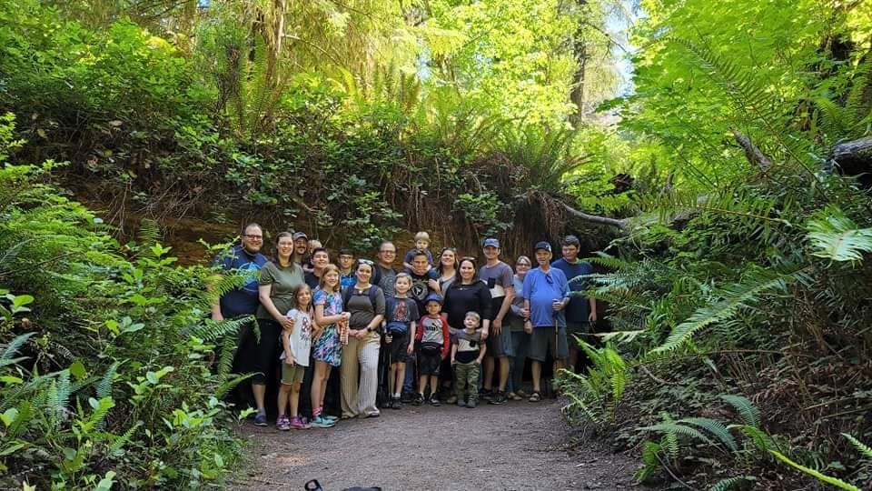Large group photo of wedding guests gathered in a lush green garden setting.