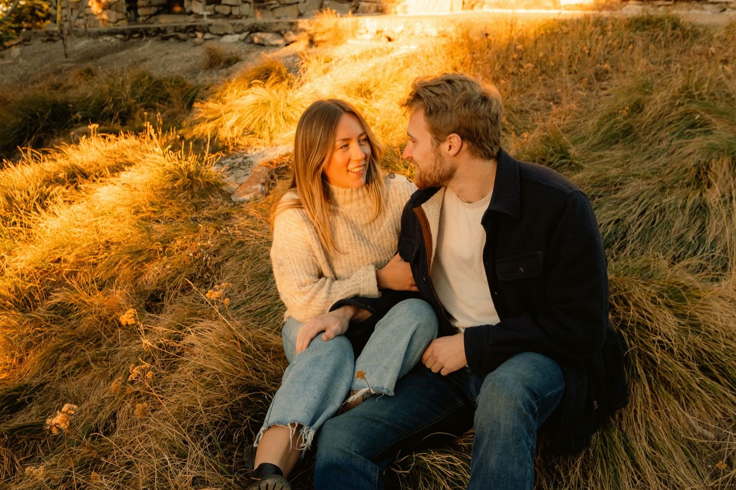 Romantic couple sitting in golden grass during sunset.