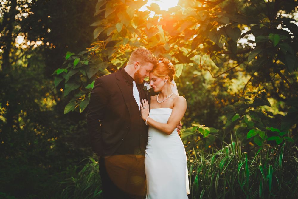A couple sharing an intimate moment in a forest setting with golden sunlight filtering through the trees. Perfect wedding portrait photo